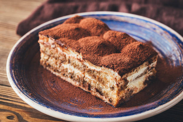 Une part de tiramisu saupoudré de cacao sur une assiette en céramique.